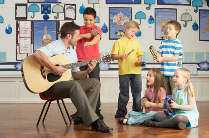 Male Teacher Playing Guitar With Pupils Having Music Lesson In Classroom